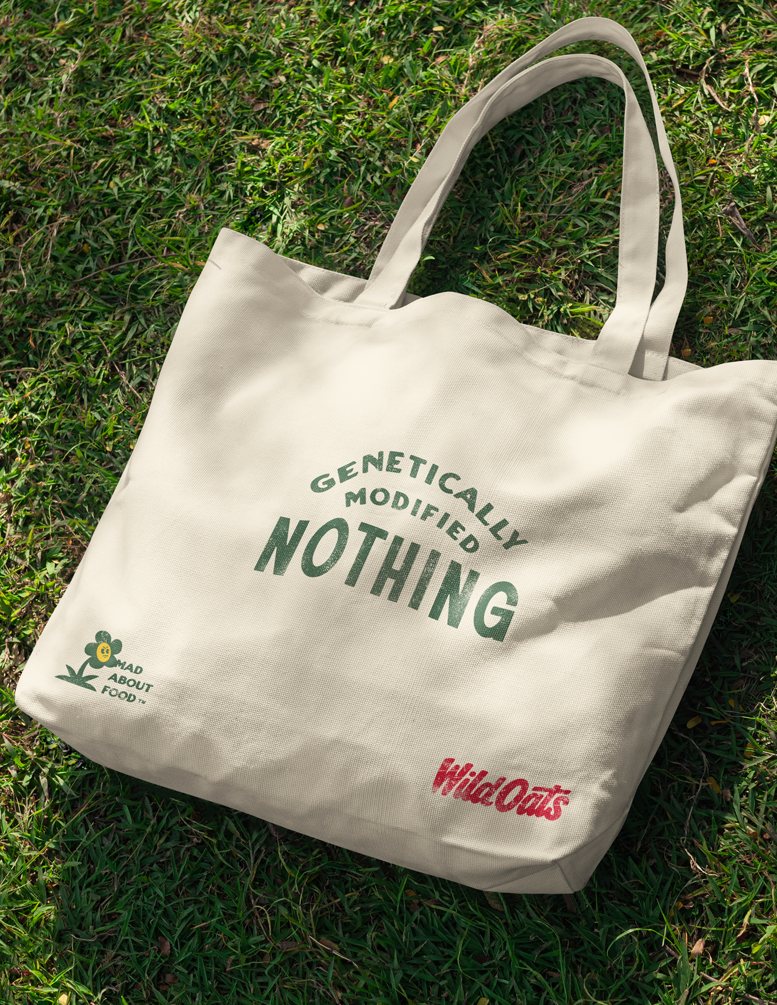 Beige tote bag on grass with text 'Genetically Modified Nothing' and logos for Mad About Food and Wild Oats.