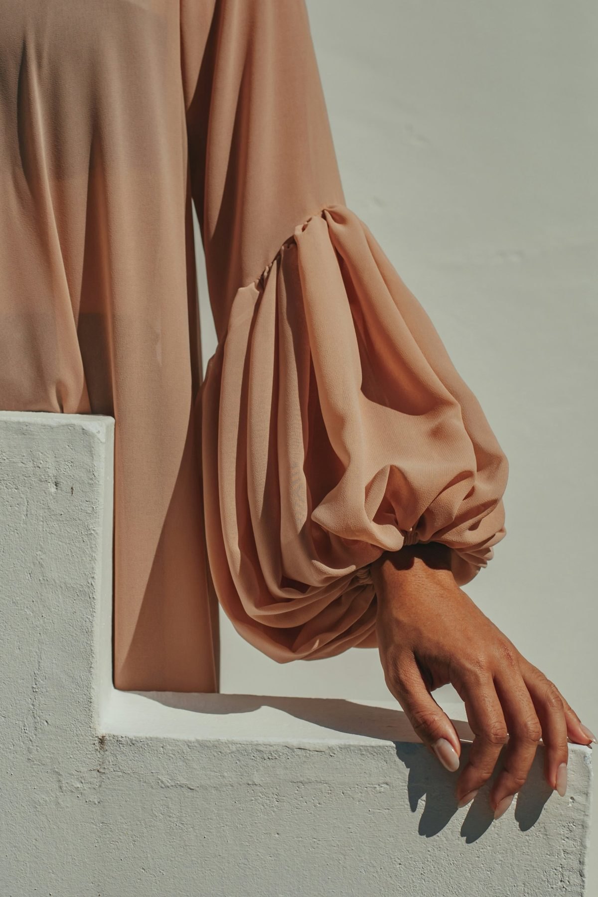 Blush chiffon balloon sleeve and hand resting on white plaster