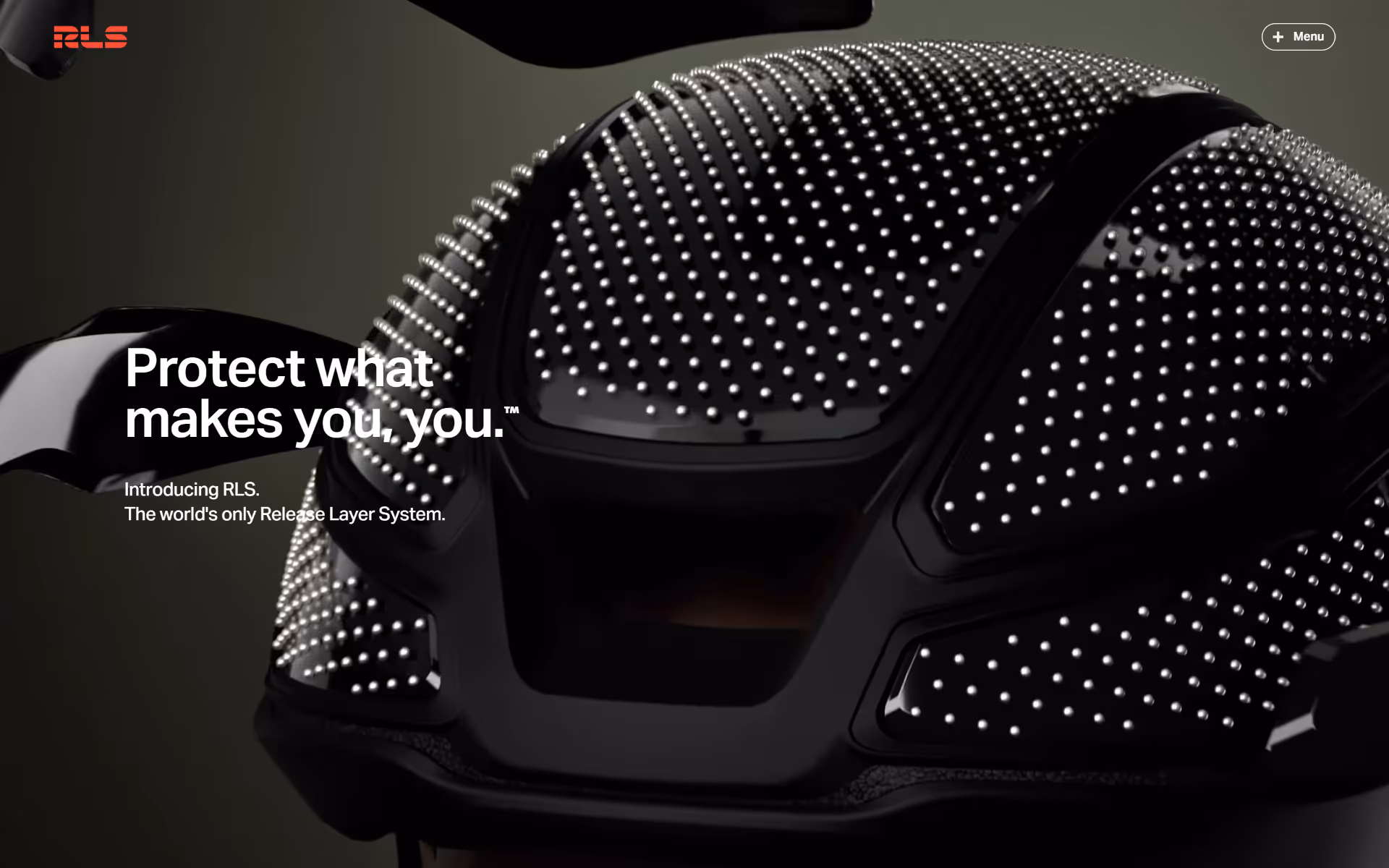 Close-up of a black protective helmet covered with small reflective dots, with text 'Protect what makes you, you. Introducing RLS, the world's only Release Layer System.'