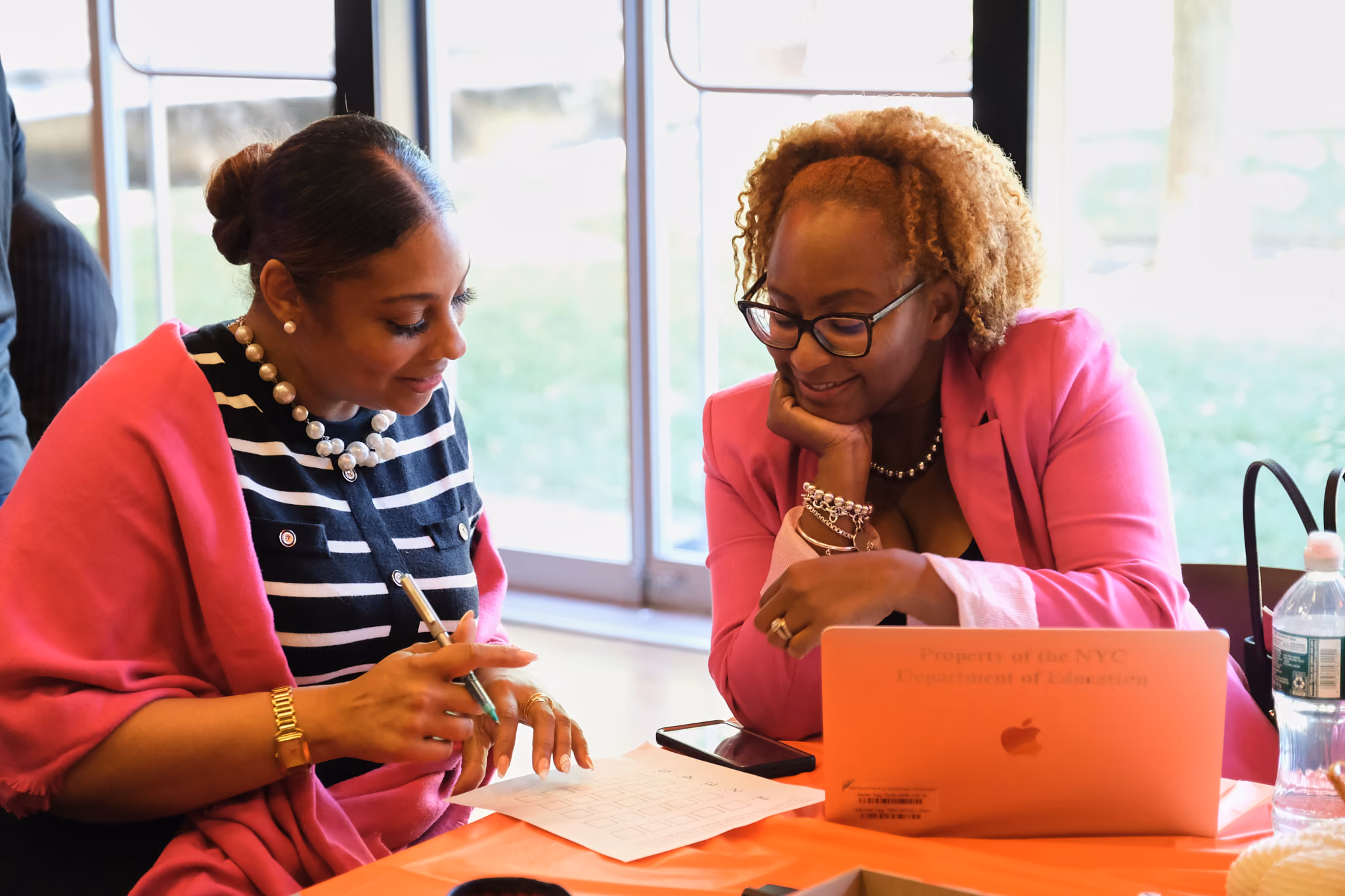Two educators collaborating over documents and a laptop at a meeting