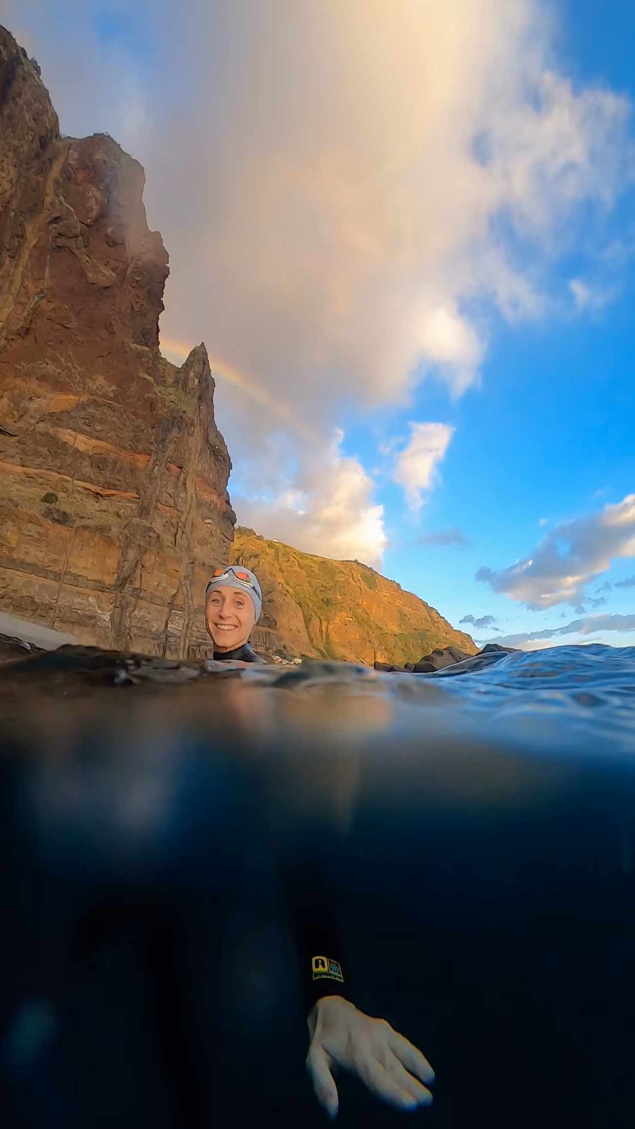 A swimmer treading water in Madeira, under a rainbow