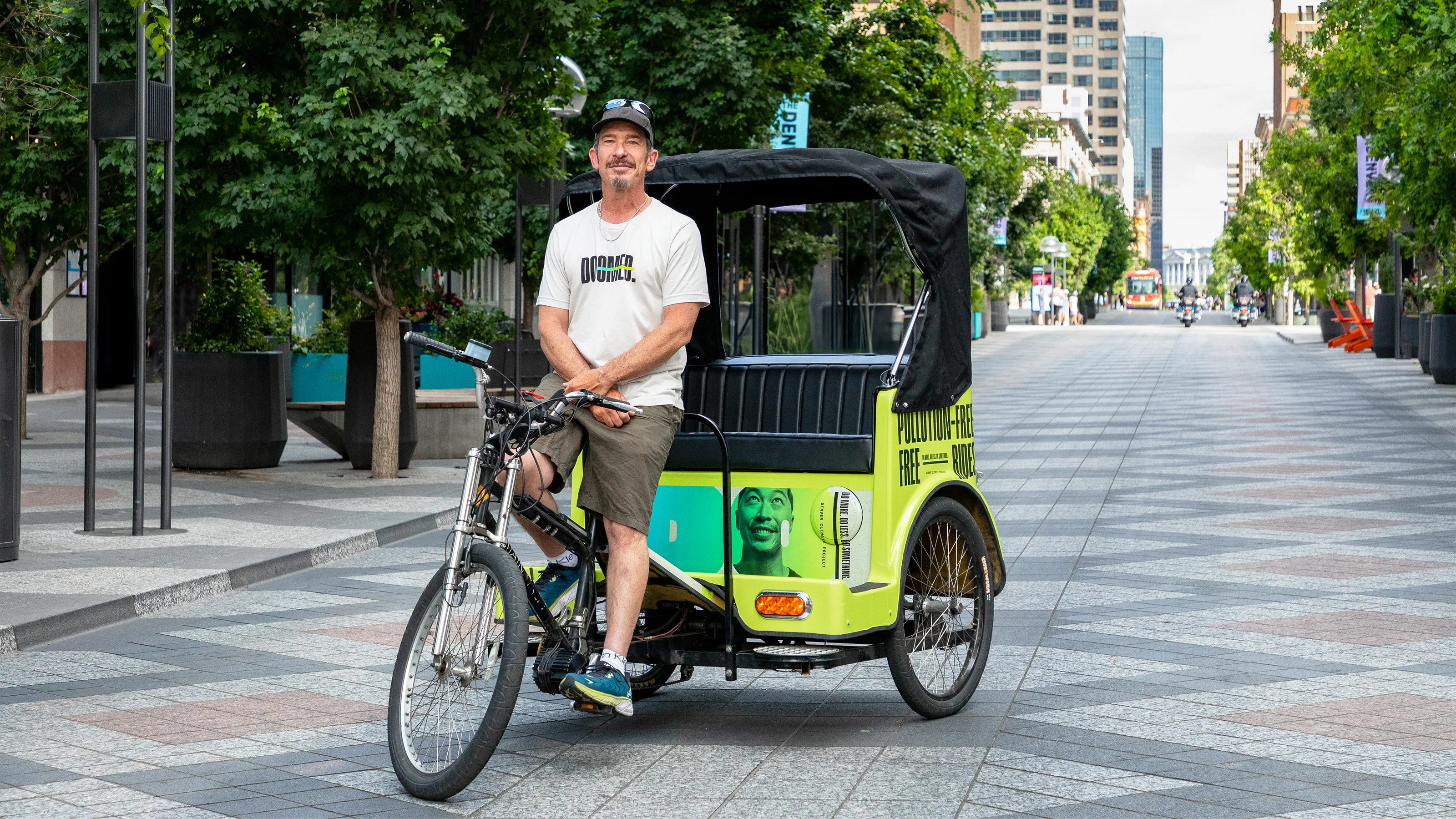pedicab driver smiling posing in front of a large outdoor tree-lined street