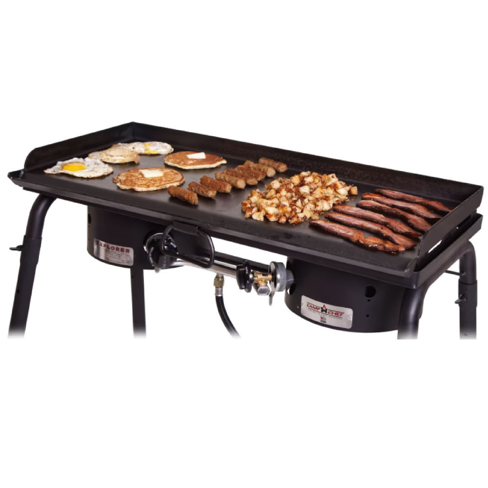 Black griddle with pancakes, bacon and eggs being cooked on it