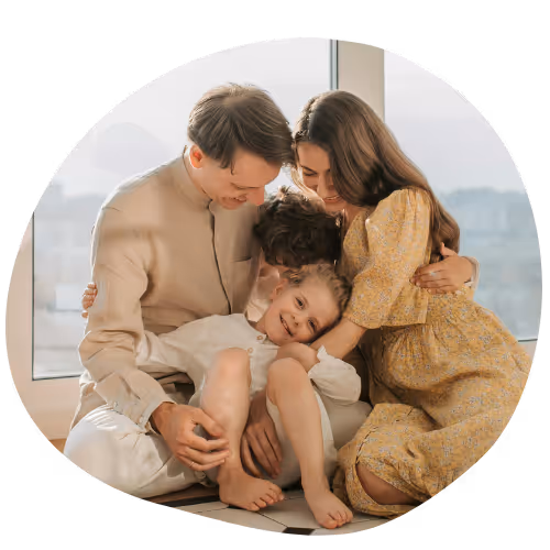 Glückliche Familie mit zwei Kindern umarmt sich sitzend vor einem Fenster.