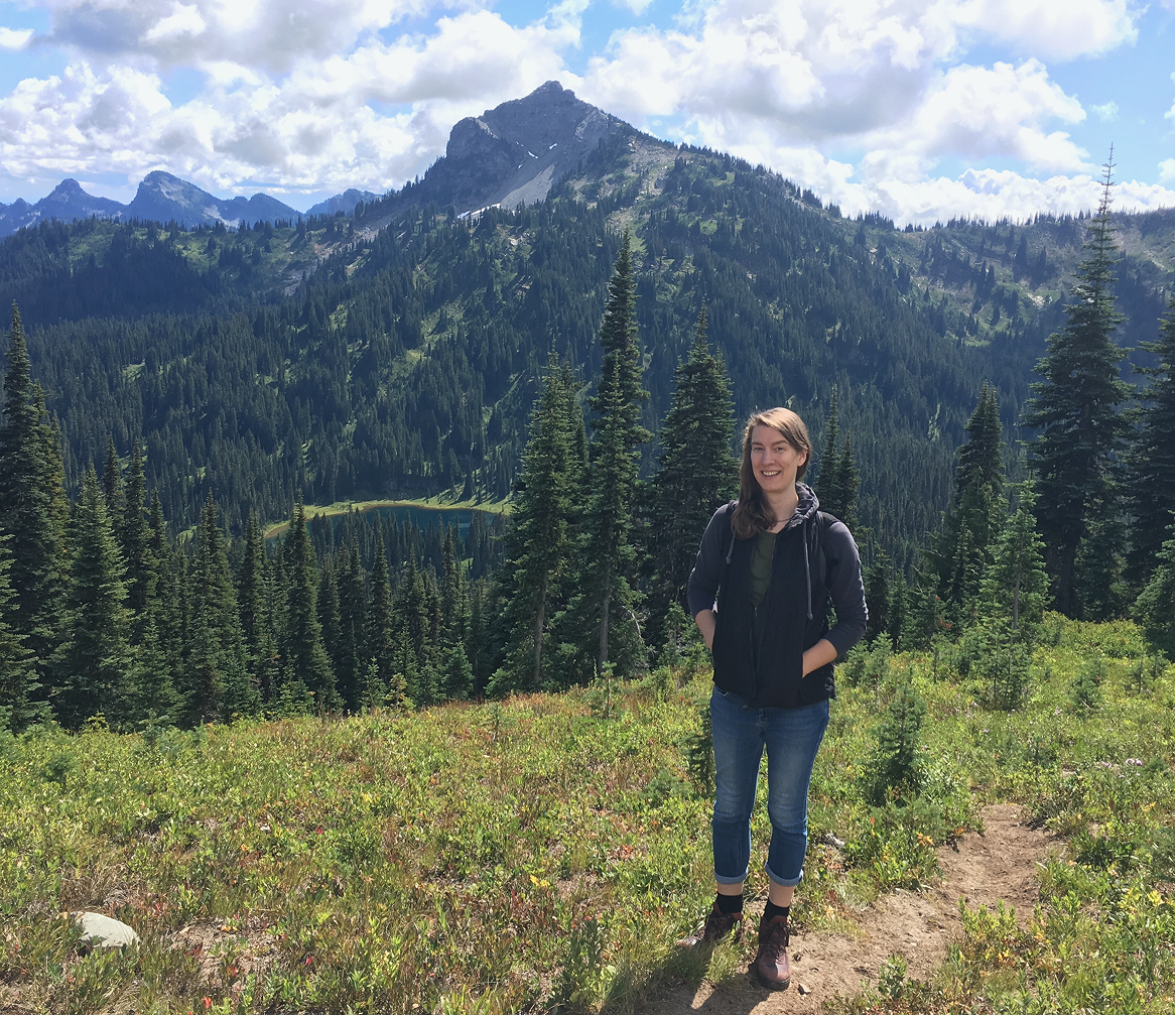 Tana Green standing on a mountain trail below a rocky peak