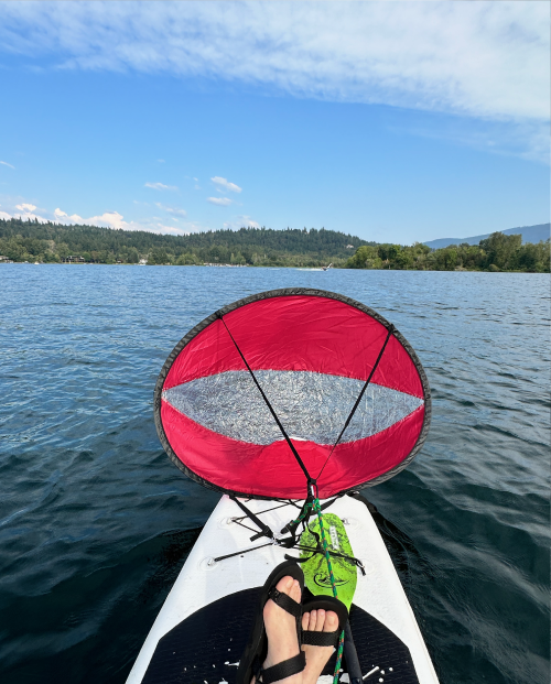 A red and white kayak sail above open water and paddle board. Feet crossed.