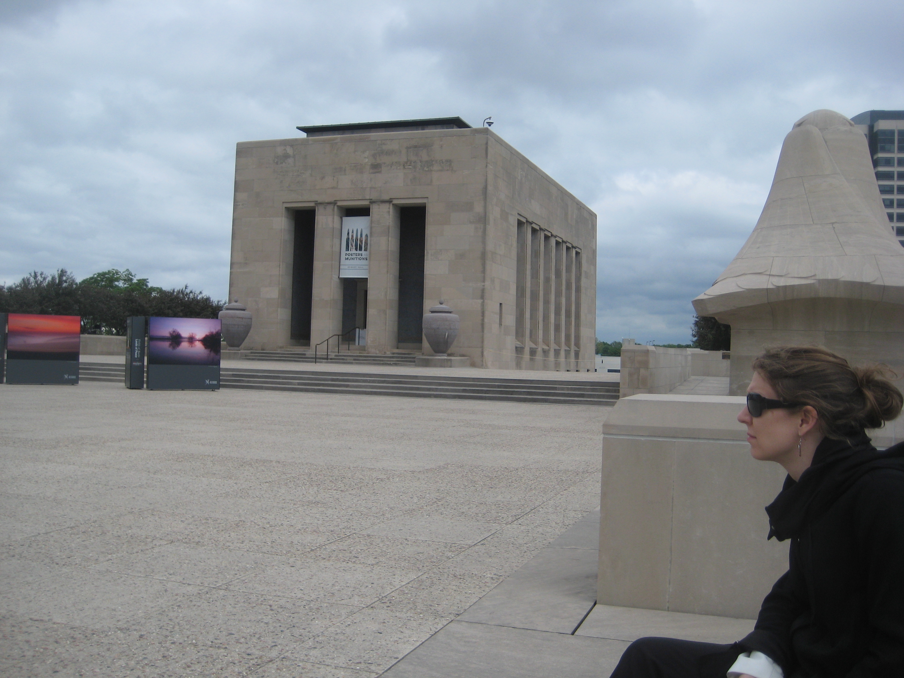 Tana Green seated on the limestone plaza above the National WWI Museum, with the Memorial's colonnaded hall behind her.