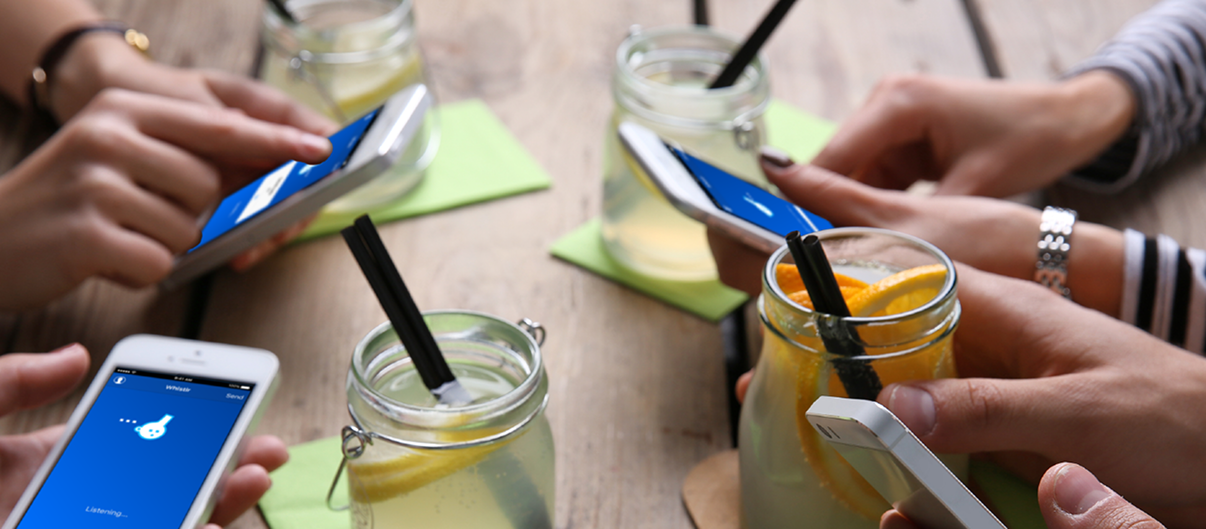 Four people around a table with lemonade jars, each holding an iPhone running Whistlr to trade contact details.