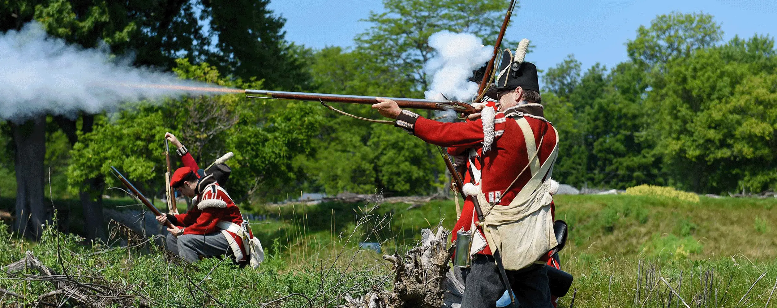 Action shot of Fort Erie Annual Siege Reenactment featuring two men in old uniforms shooting off historical guns outside