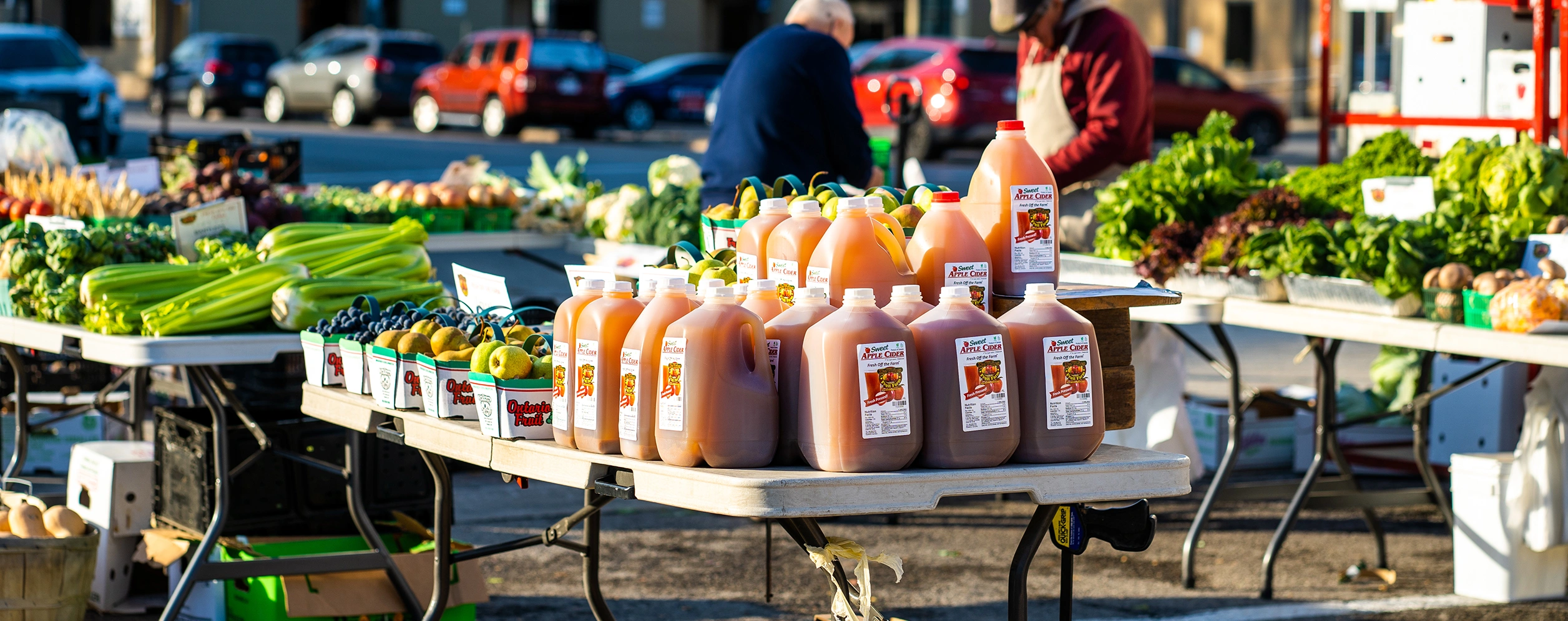 Port Colborne Farmers' Market with tables lined with vegetables and apple cider with patrons in background