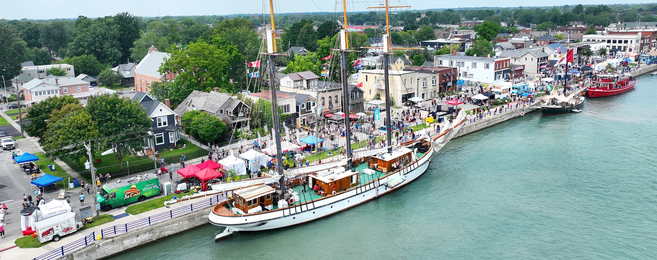 Aerial shot of boat docked along canal lined with vendors and patrons representing Canal Days Marine Heritage Festival