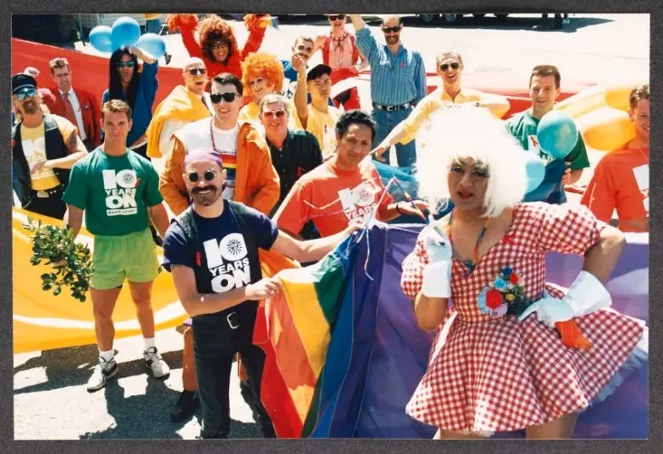 A group in colourful 1990s dress holding a rainbow flag at the Devotion Festival, 1993