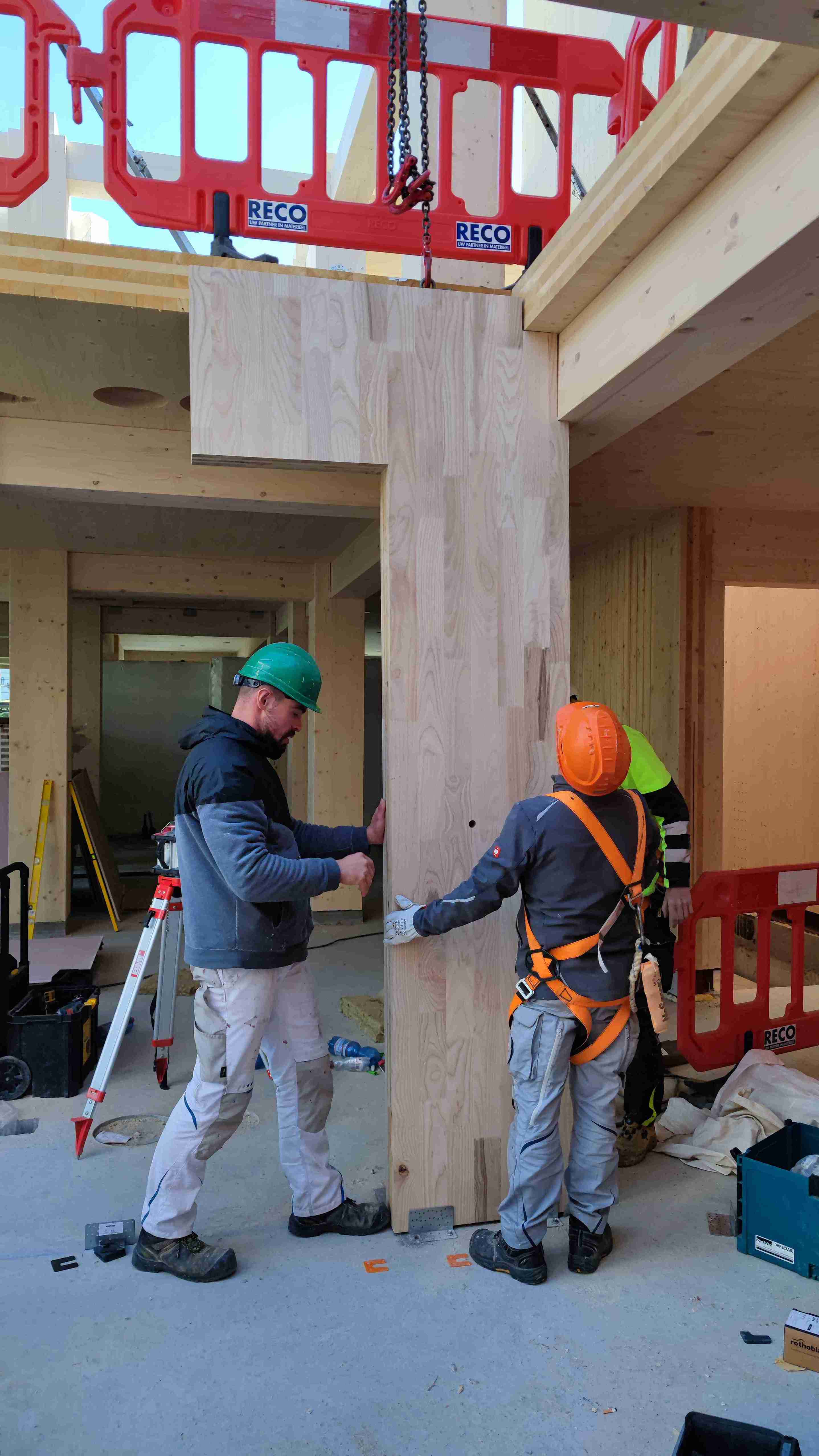 Bouwplaats waar C-CLT-constructies worden gemonteerd; twee bouwvakkers werken rondom de houten kolommen en liggers met ladders en gereedschap.