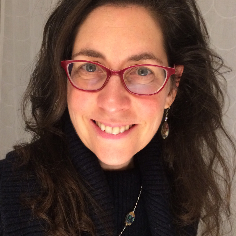 Professional headshot of Jenny Ferry, a brunette woman wearing red glasses, jewelry and a black sweater.. 