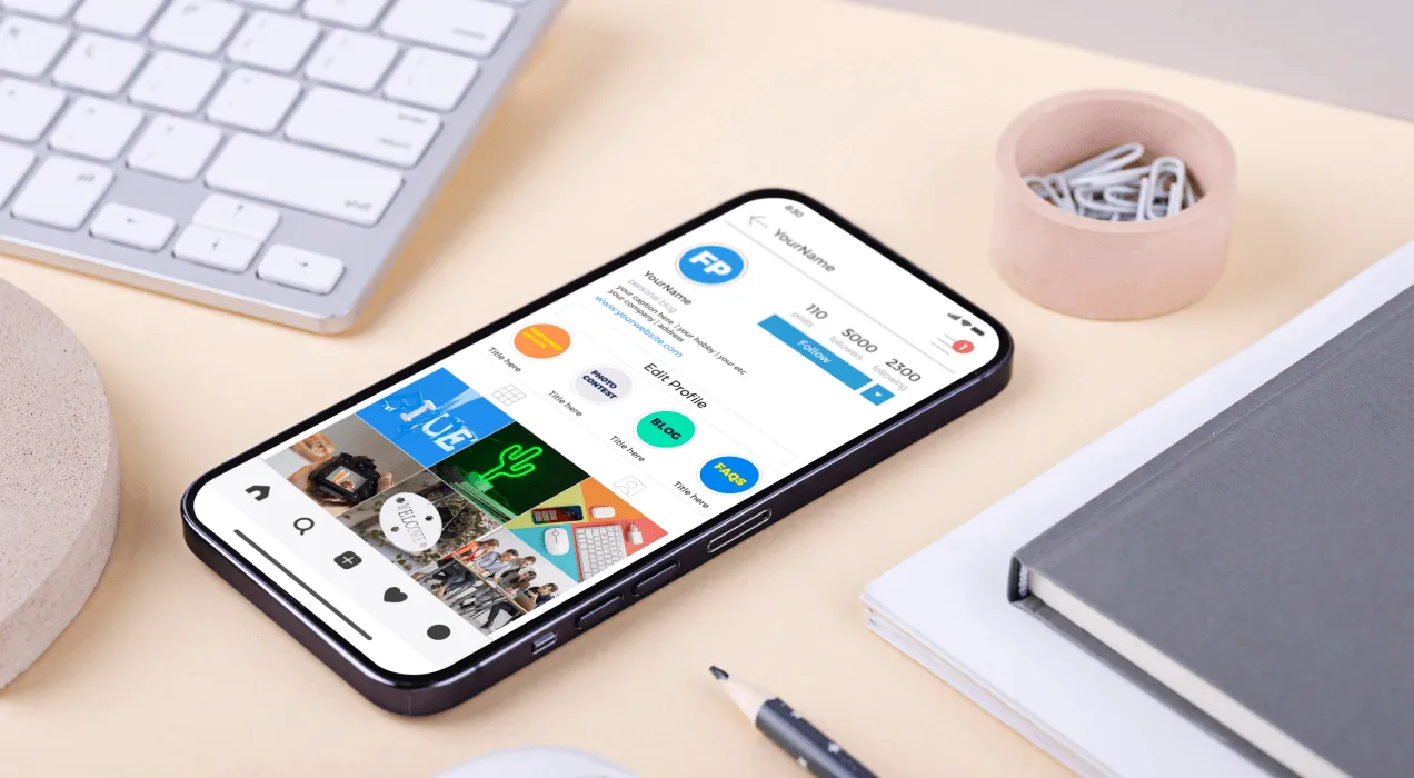 A smartphone with social media app icons displayed on the screen, placed on a desk beside a keyboard, an earphone case, and a notebook.