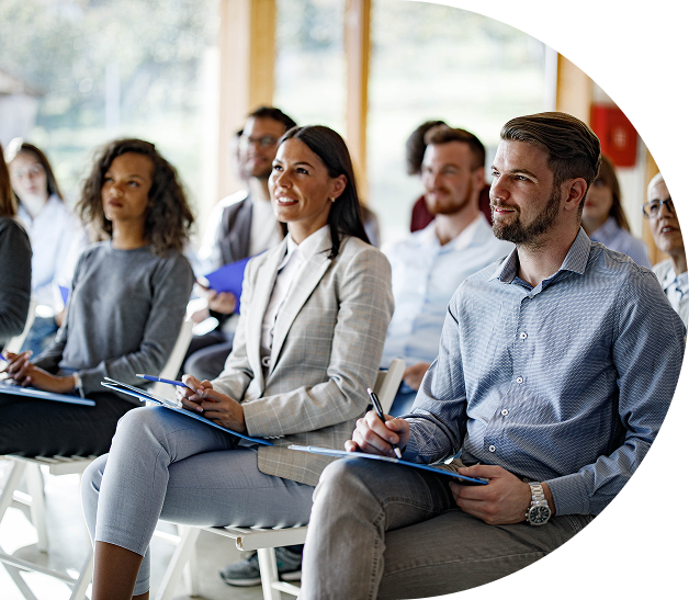 Professionals intently listening at a conference, taking notes on notepads