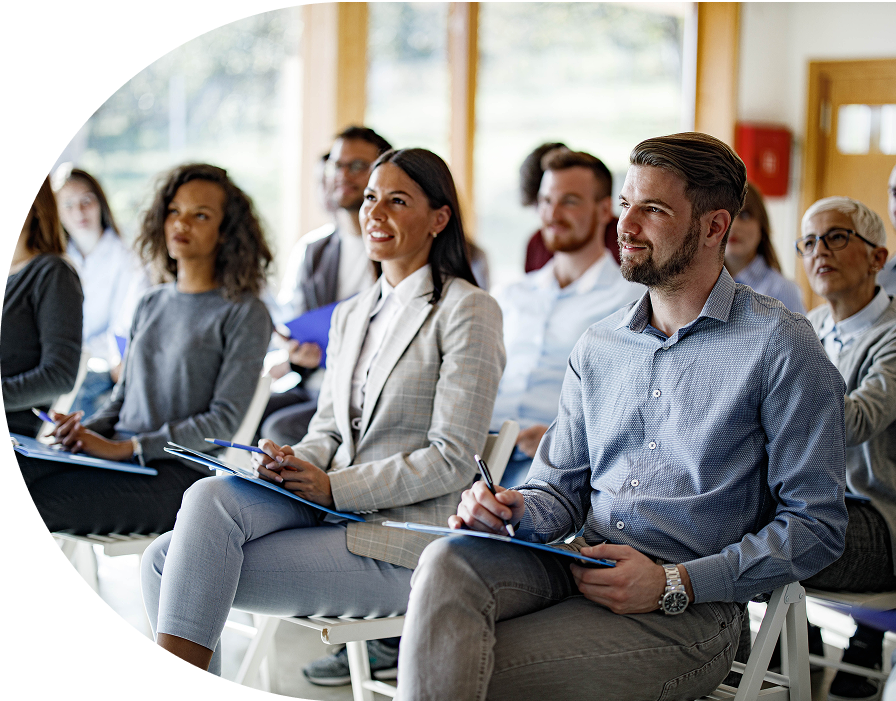 Professionals intently listening at a conference, taking notes on notepads