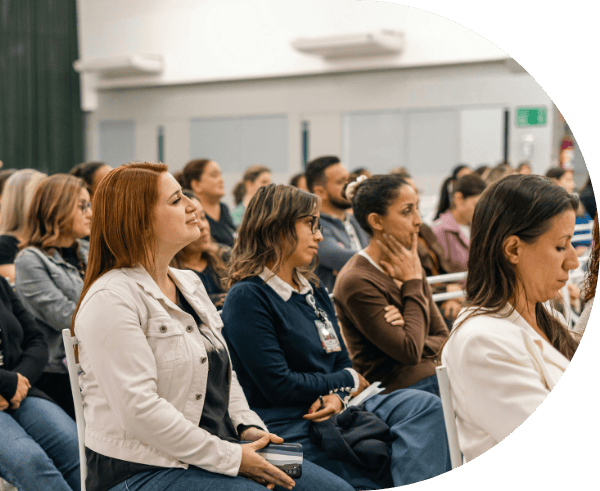 Professionals intently listening at a conference, taking notes on notepads