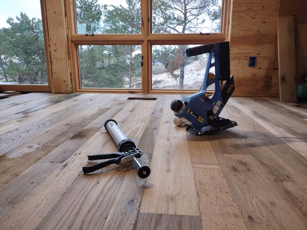 Hardwood flooring and installation tools beside large windows