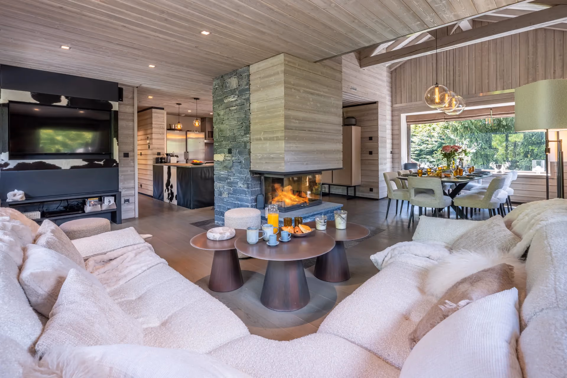 Salon avec cheminée centrale, cuisine ouverte et salle à manger du Chalet Mozart, chalet de luxe à Megève.
