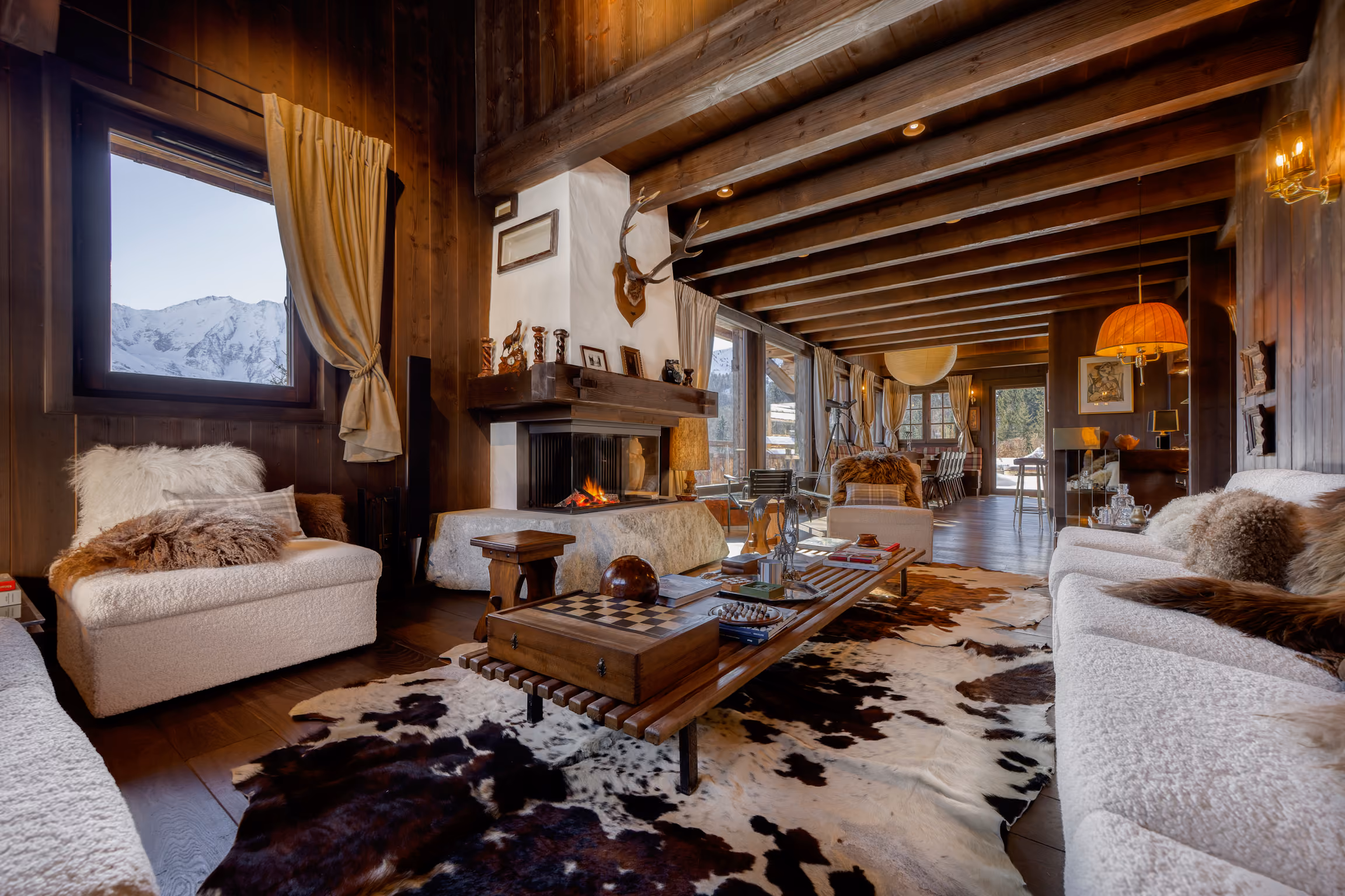 Salon chaleureux avec cheminée, grandes baies vitrées et décoration raffinée dans un chalet de luxe à Saint-Gervais Mont-Blanc.