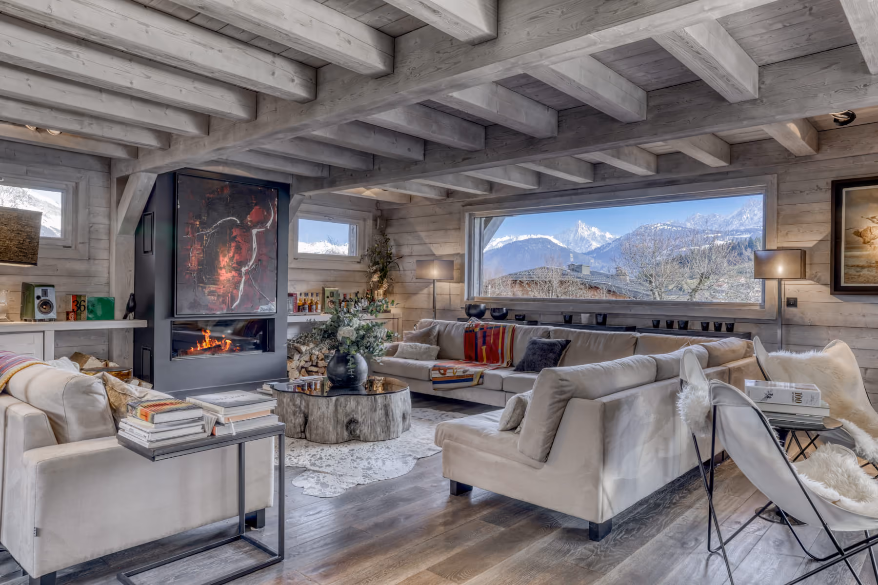 Spacious living room with contemporary fireplace and panoramic views of the Mont Blanc massif in a luxury chalet.