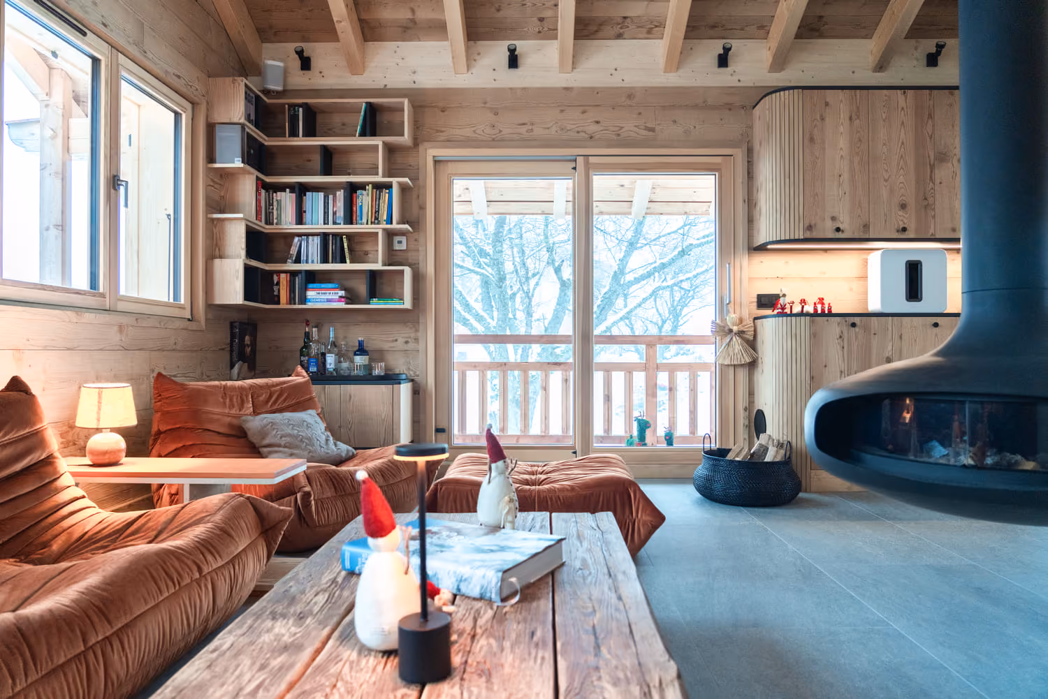 Cozy lounge with suspended fireplace, built-in bookshelves and access to the chalet balcony.