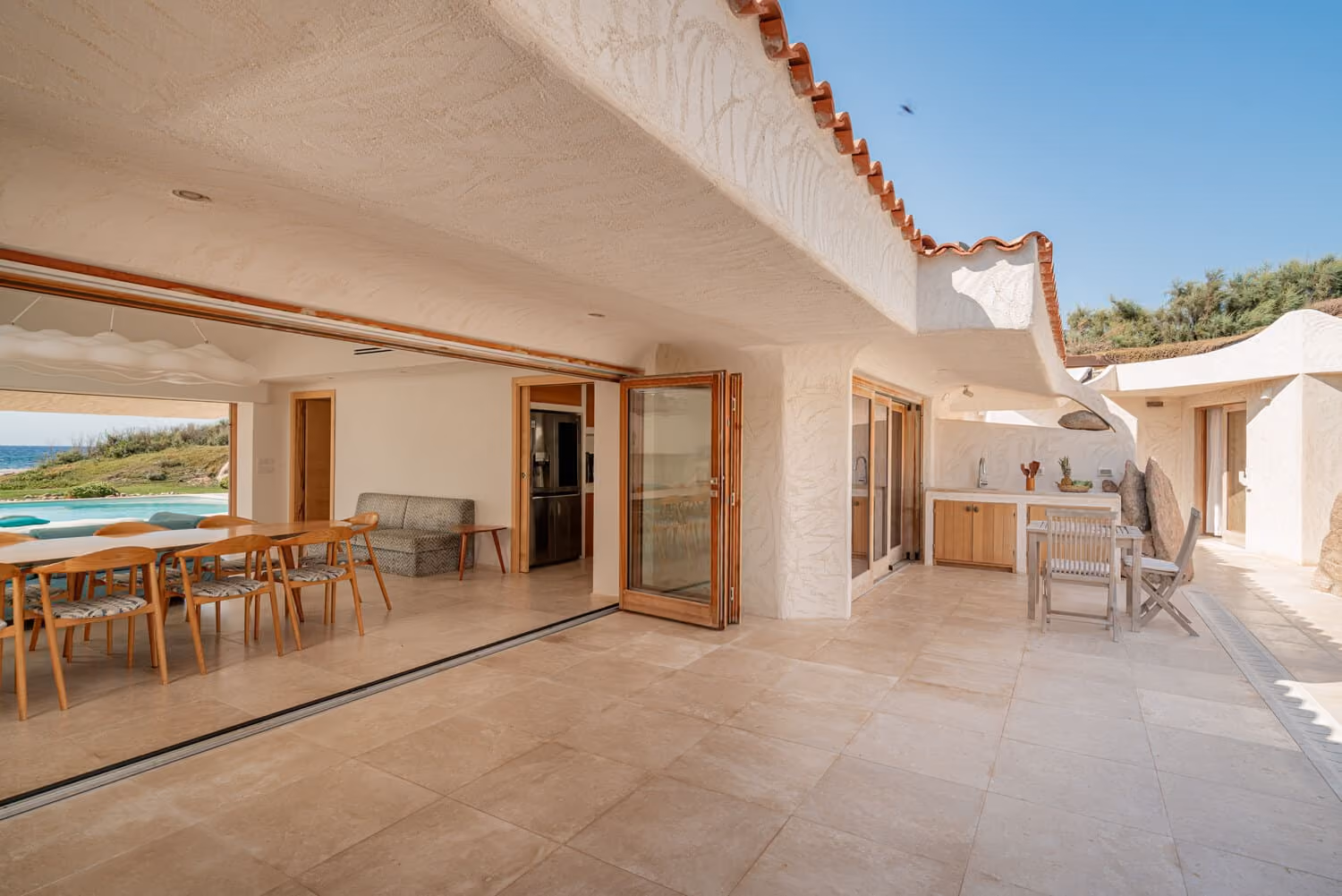 Spacious covered terrace connecting the living areas to the pool in a beachfront villa in Sardinia.
