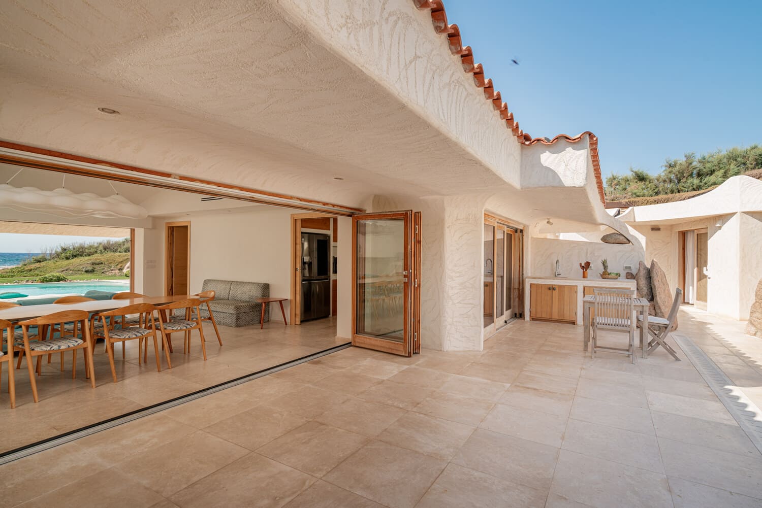 Grande terrasse couverte reliant les espaces de vie à la piscine dans une villa pieds dans l'eau en Sardaigne.
