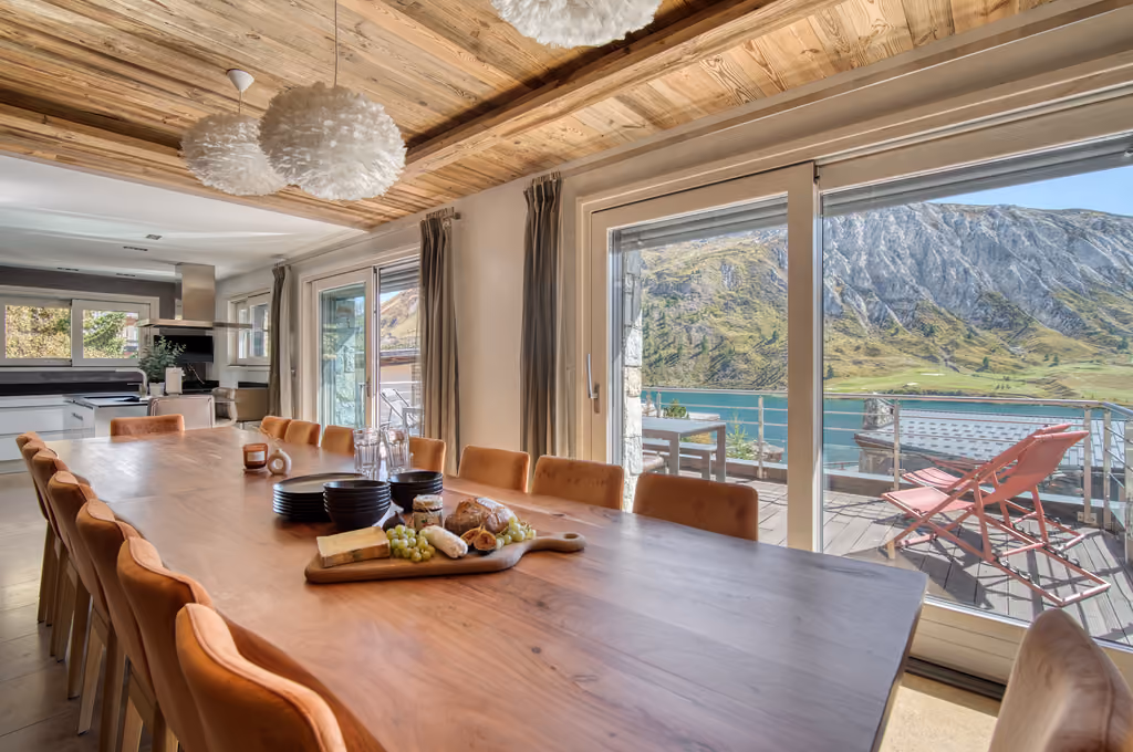 Grande salle à manger du Chalet Ancolie avec vue panoramique sur le lac de Tignes et accès direct à la terrasse