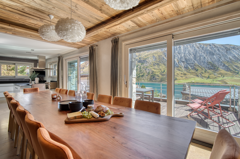 Grande salle à manger du Chalet Ancolie avec vue panoramique sur le lac de Tignes et accès direct à la terrasse