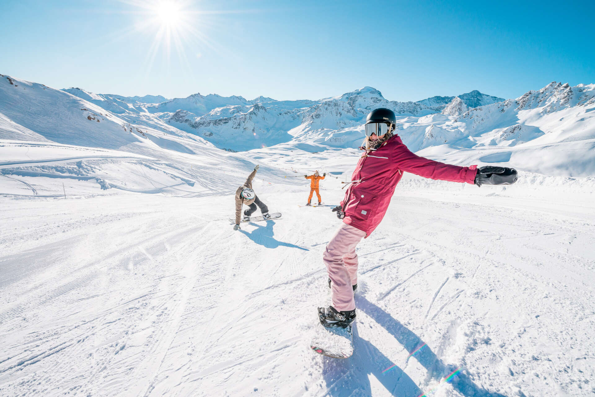 Snowboarders enjoying the pristine slopes of the Tignes–Val d'Isère ski area under clear blue Alpine skies.