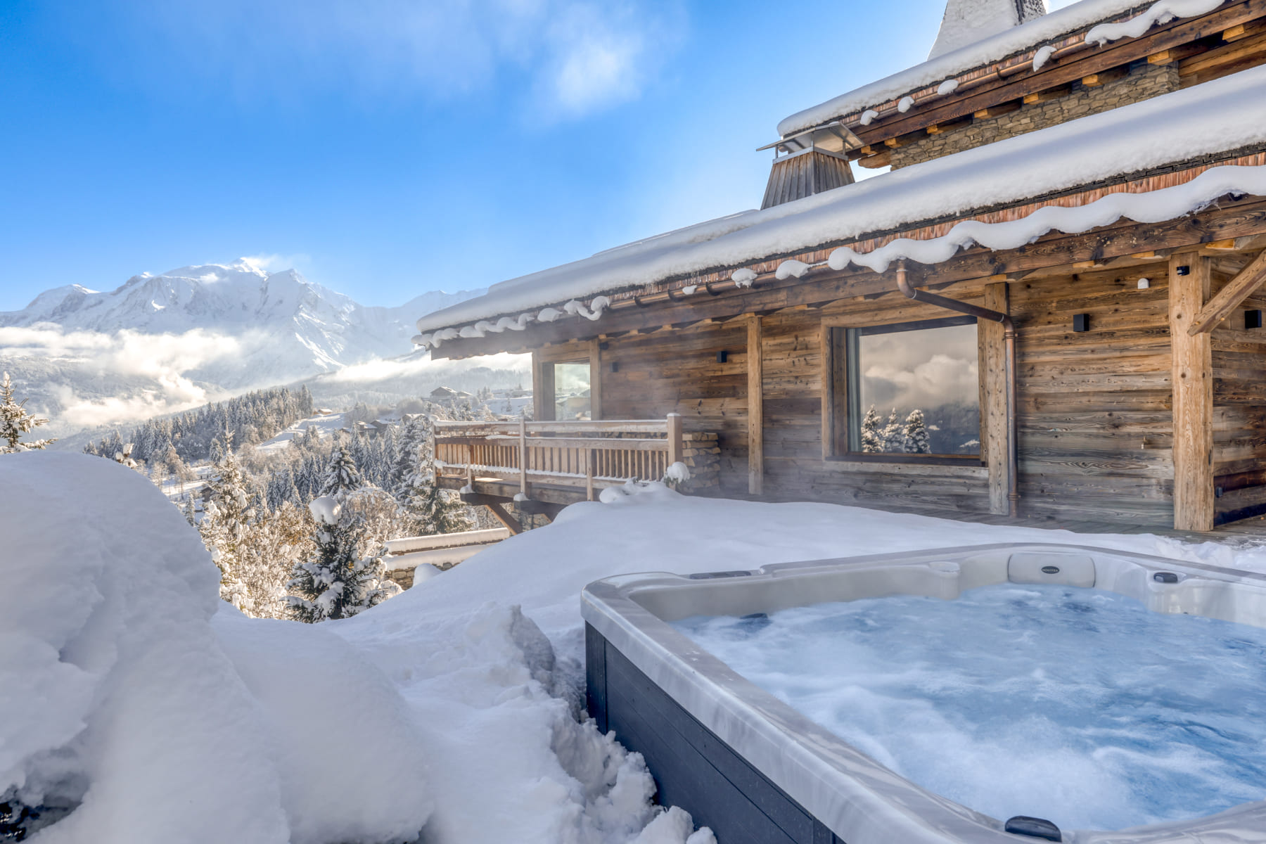 Jacuzzi extérieur dans la neige face au massif du Mont-Blanc depuis un chalet alpin.