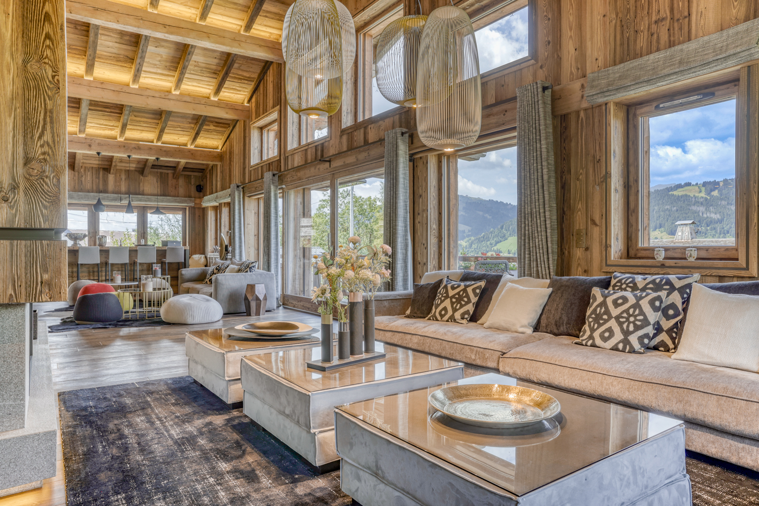 Grand salon lumineux d’un chalet en bois avec baies vitrées et vue sur les montagnes