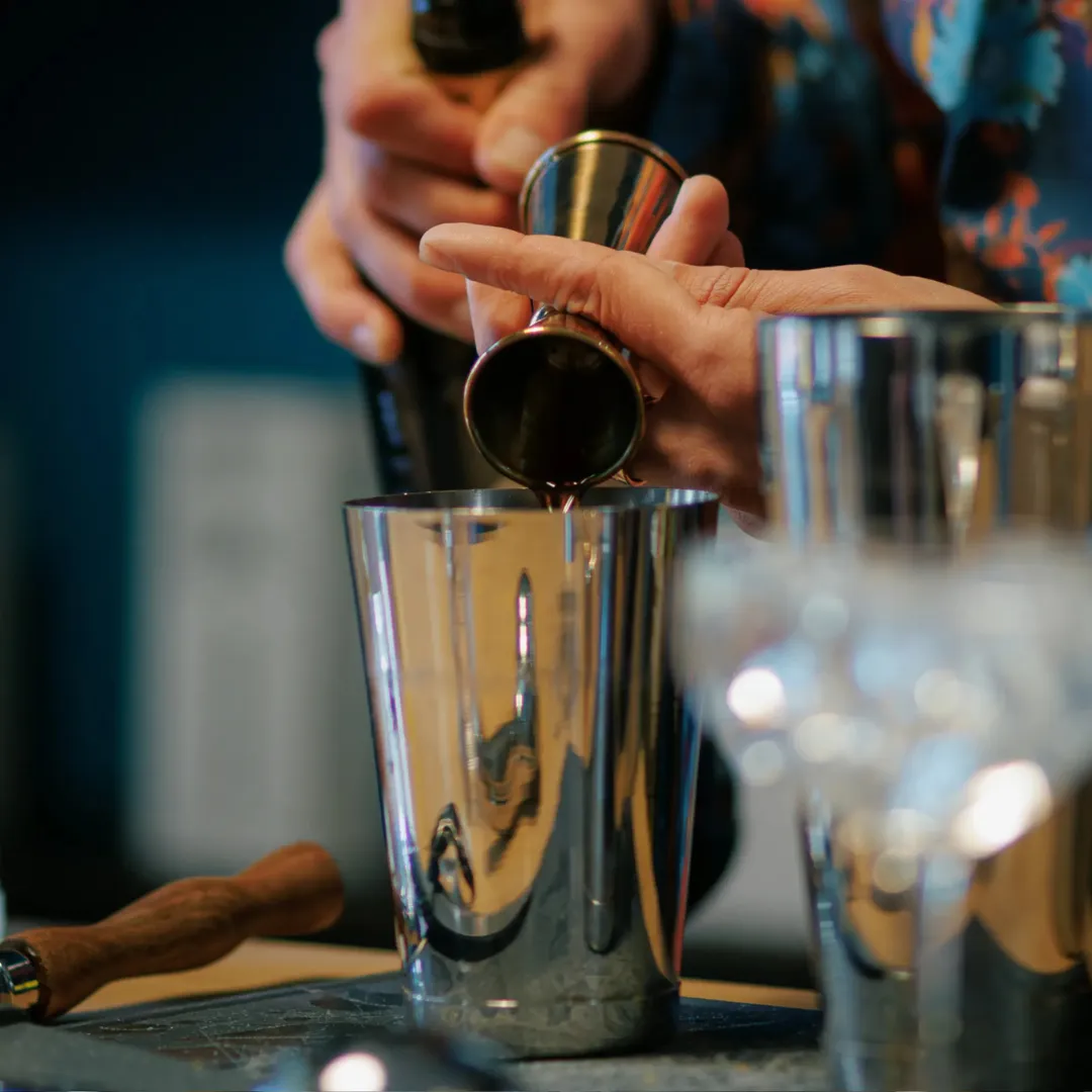 hands pouring a liquid in a mixing glass