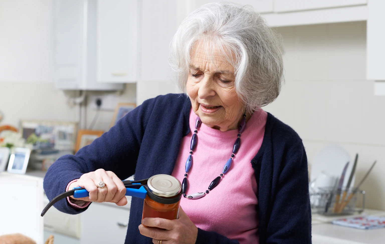 Older woman using a jar opener in a kitchen, demonstrating adaptive tools used in occupational therapy for daily living tasks.