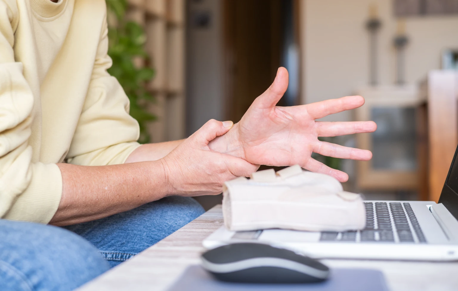 Person holding their wrist while studying on a laptop with a wrist brace nearby.