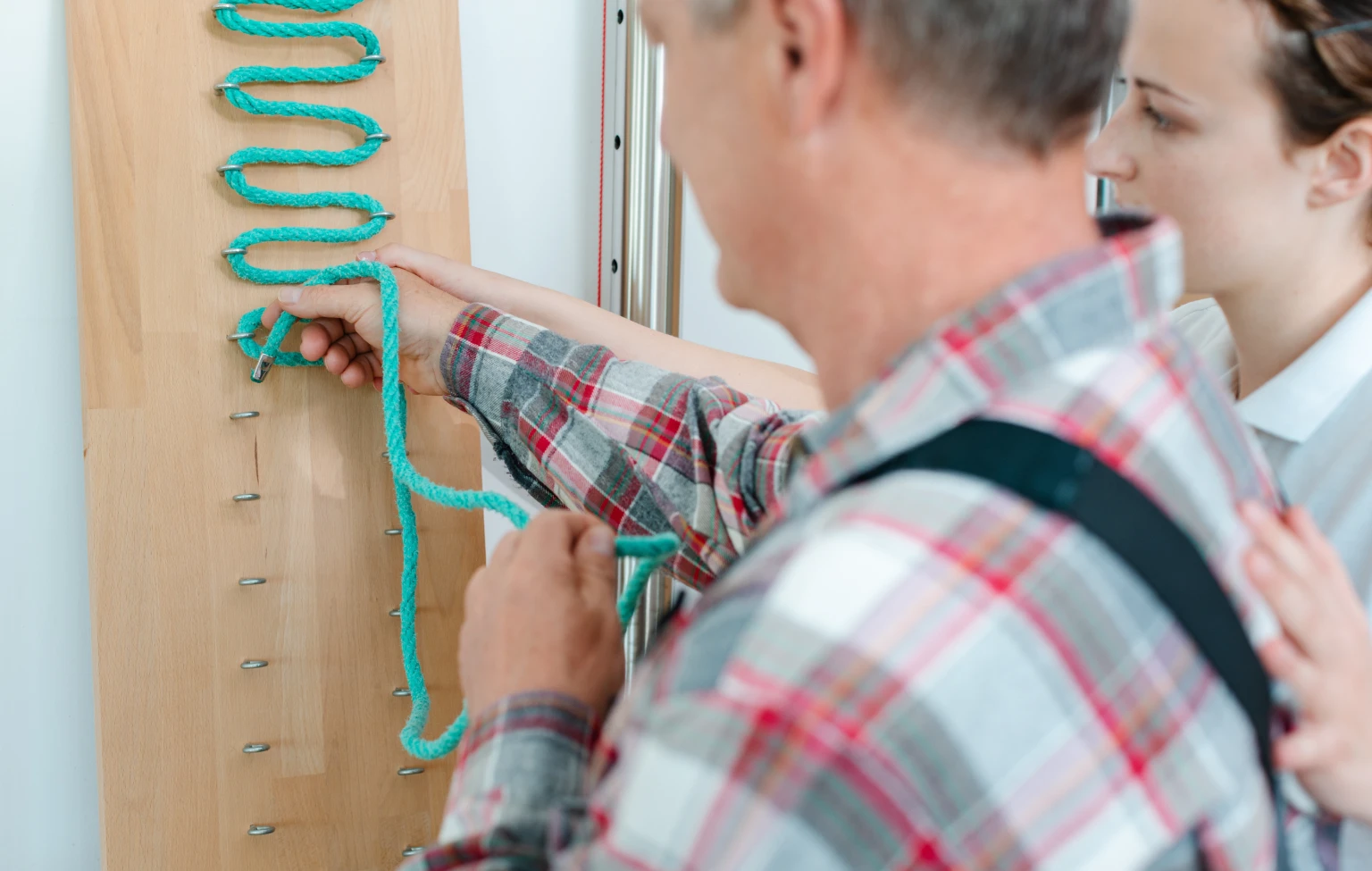 An occupational therapist guides an older adult through a fine motor skills exercise, threading a rope through pegs to improve hand coordination.