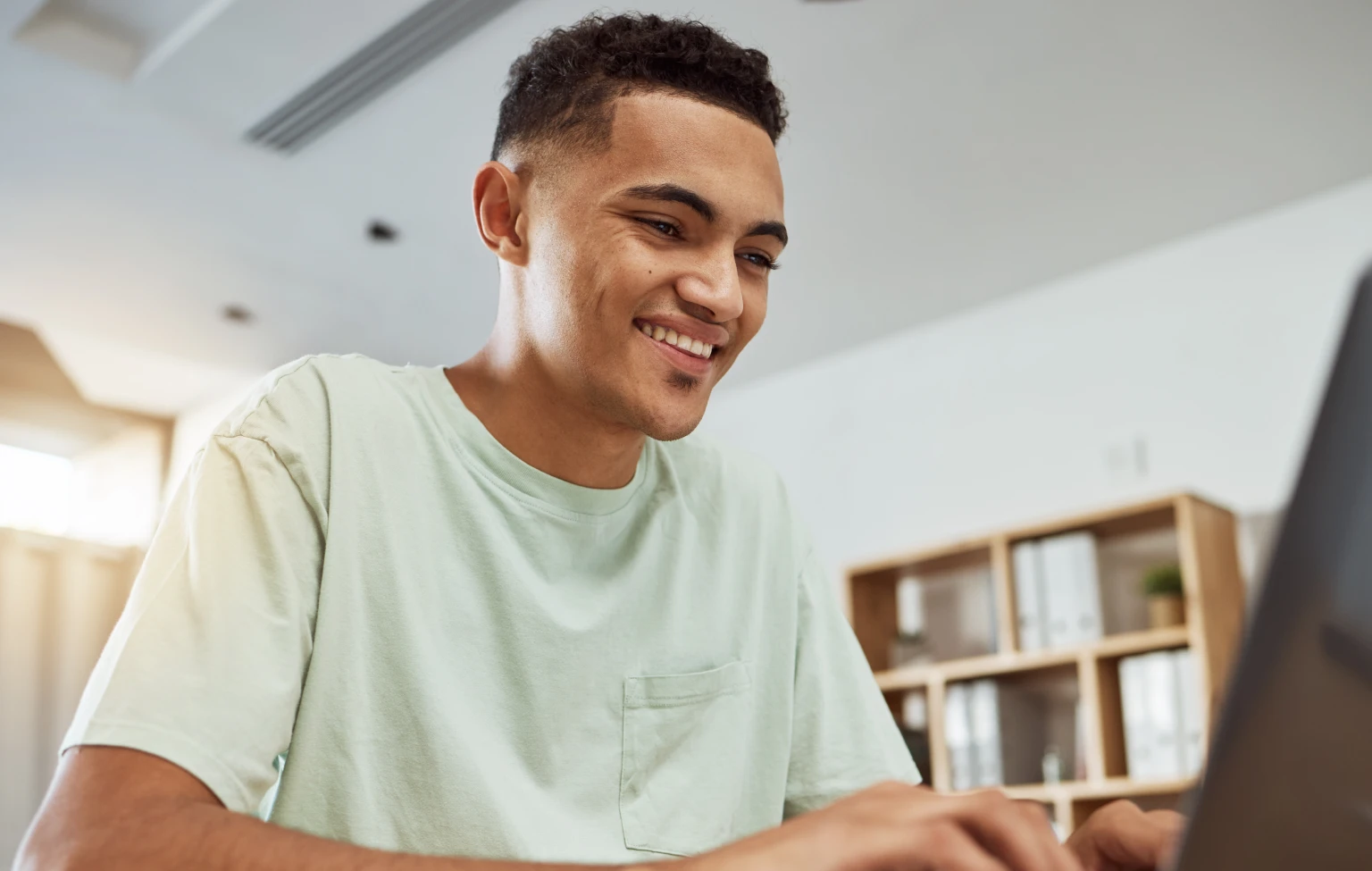 Smiling young man working on a laptop at home, appearing focused and engaged in his studies.