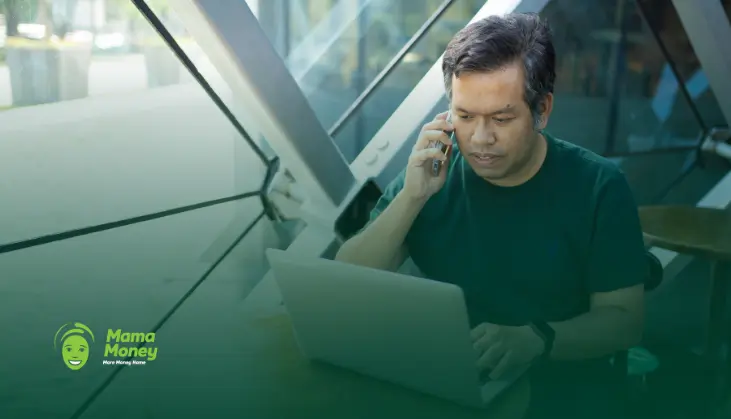 Thai expat using a laptop and mobile phone to manage banking in South Africa."
