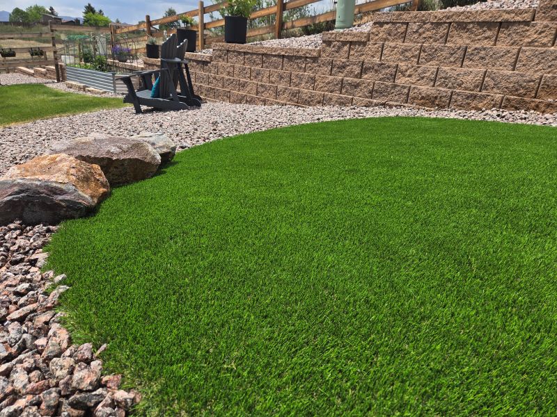 Close-up of premium artificial turf installation bordered by decorative rock and natural boulder accents in new landscape area.