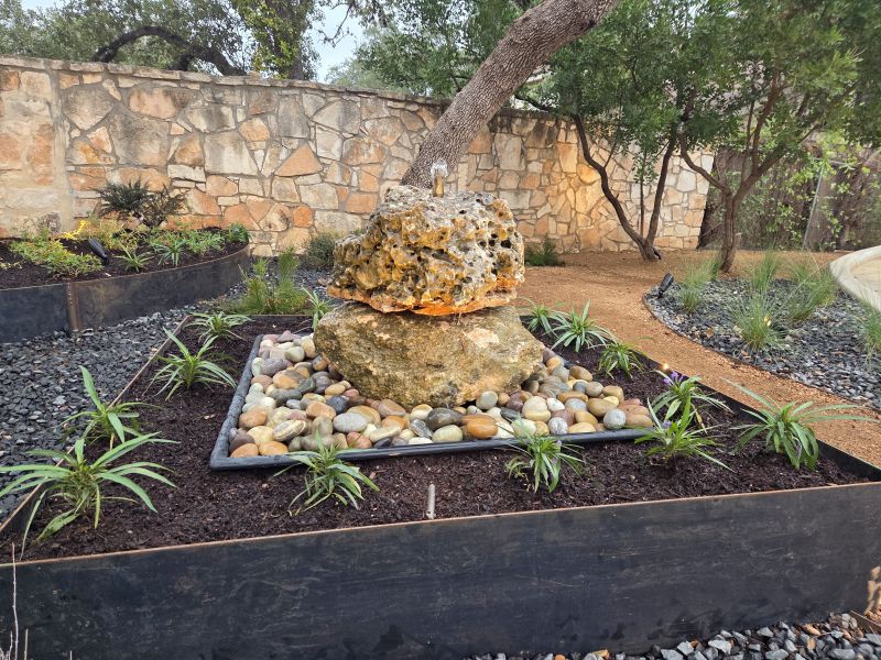 Natural limestone bubbling fountain feature installed within custom corten steel planter beds as the centerpiece of a San Antonio garden renovation.