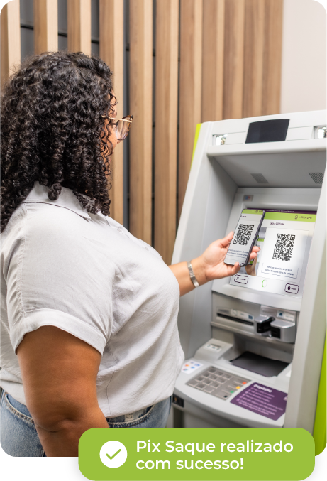 Mulher usando avental verde, de braços cruzados, em uma loja com potes de mantimentos no primeiro plano. Ao fundo, um caixa eletrônico ‘Saque e Pague’ está visível no lado direito.