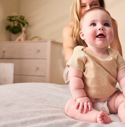 Young Baby sitting on blanket with Mom in the background