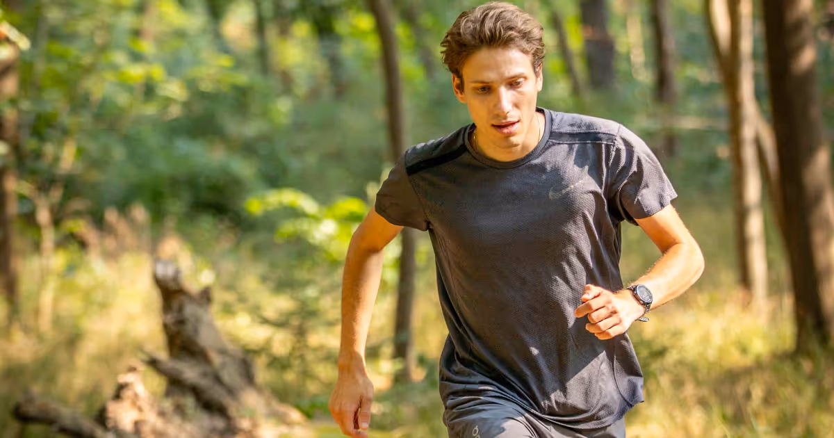 Junger Mann läuft im Wald auf einem sonnigen Weg mit grünen Bäumen im Hintergrund.