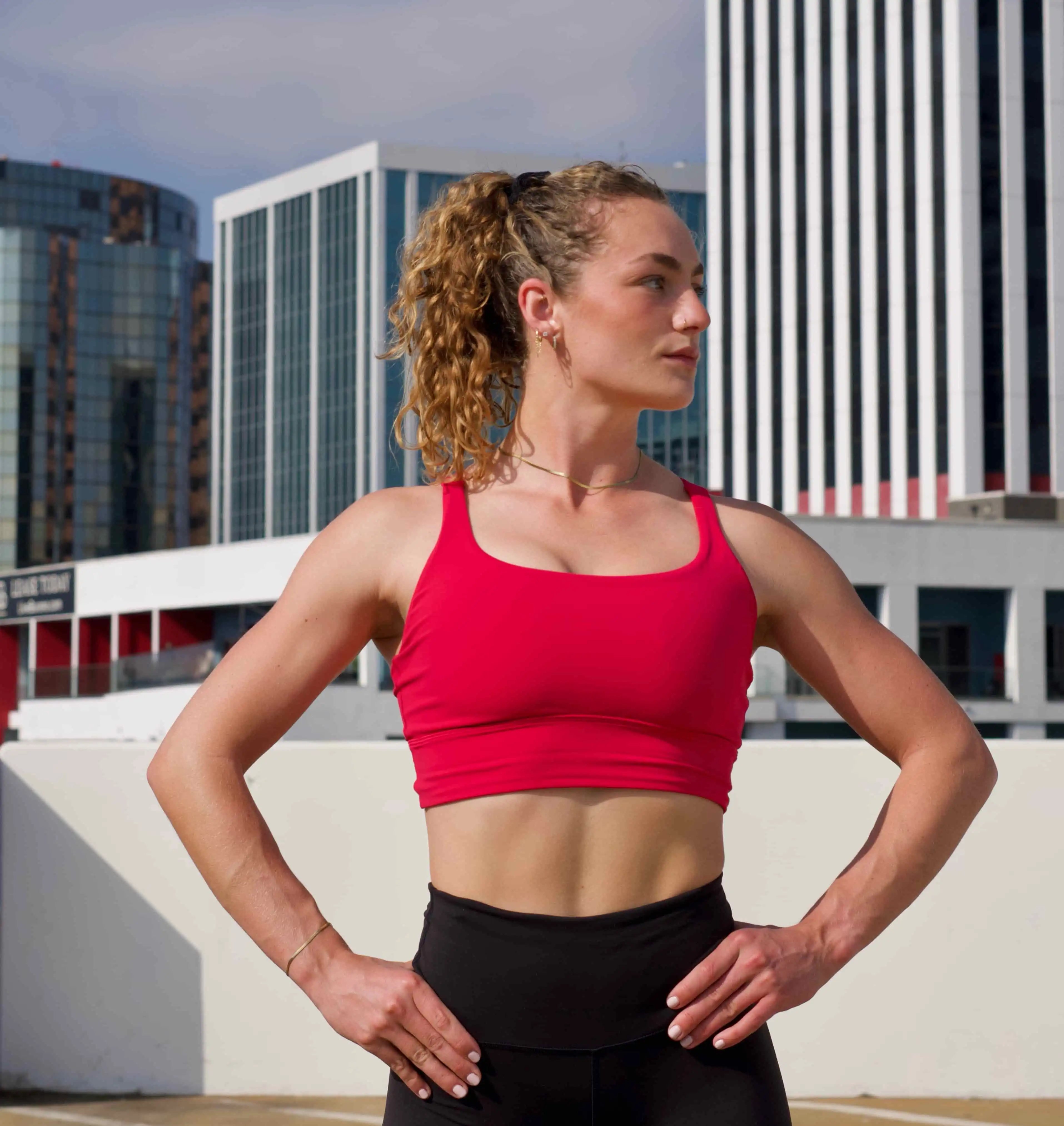 Model confidently poses with one hand on her hip, showcasing a bright pink Lululemon sports bra paired with sleek black Wunder Train leggings.