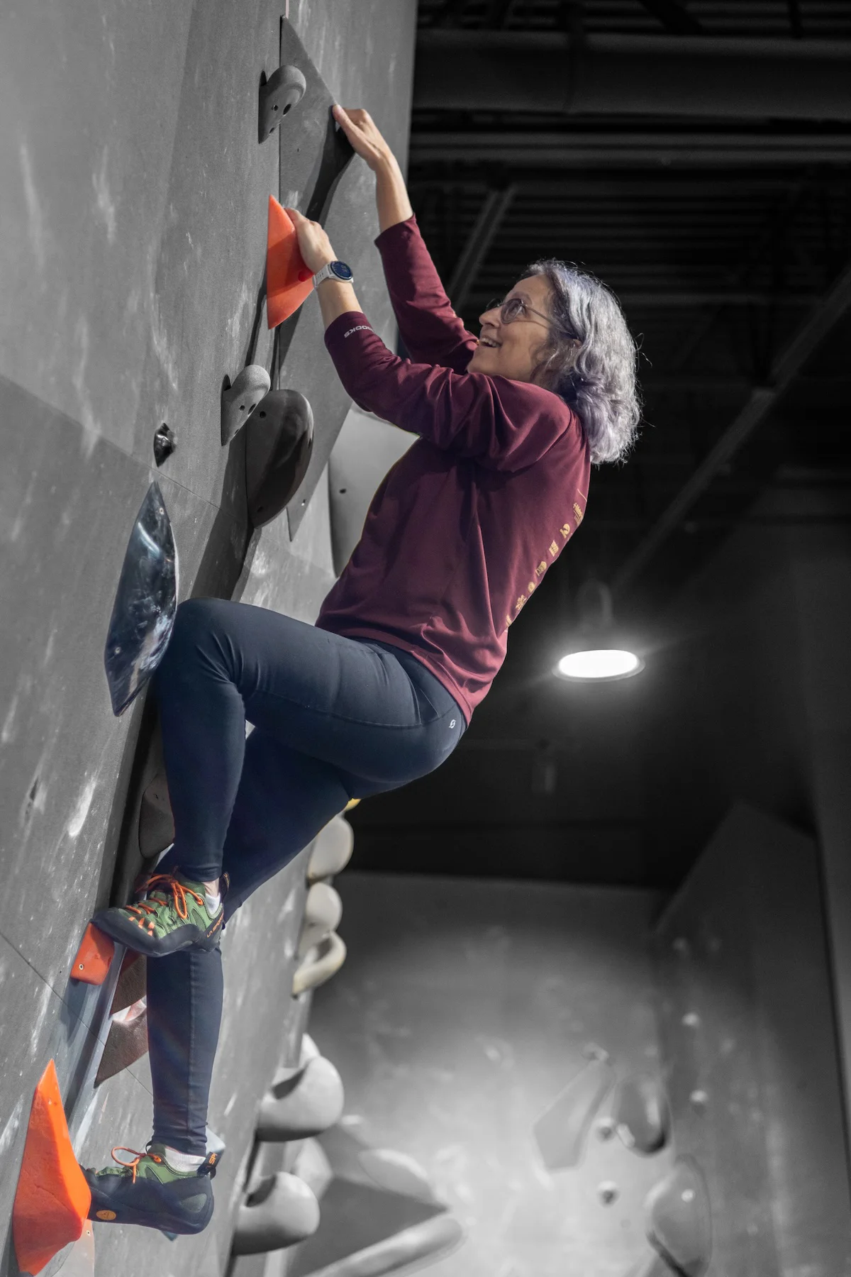 Older woman bouldering an overhang on small holds at Shift Climbing indoor climbing gym