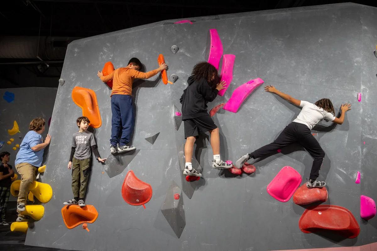 Kids climbing class bouldering across a wall on bright holds at Shift Climbing indoor gym