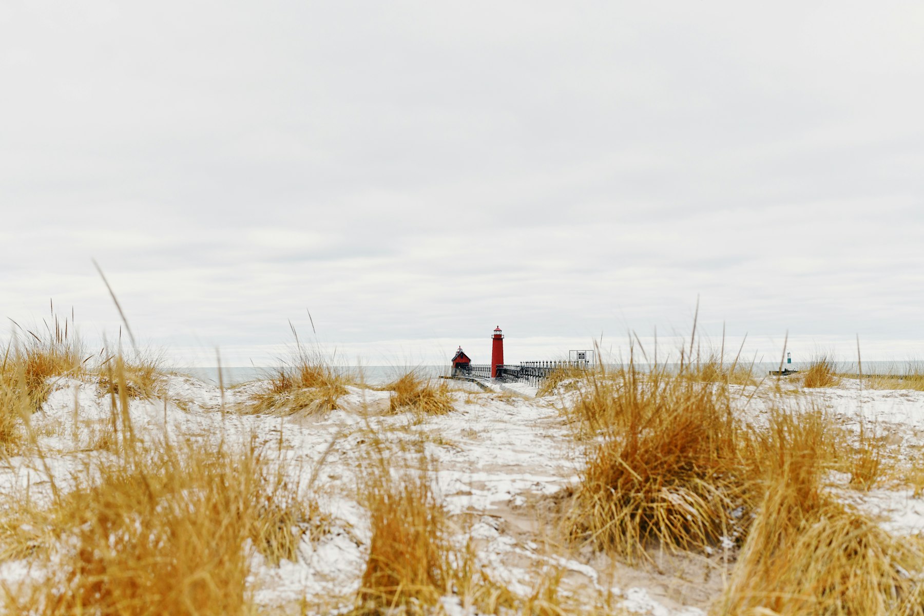 Snow-covered dunes and a red lighthouse on the Lake Michigan shore in winter