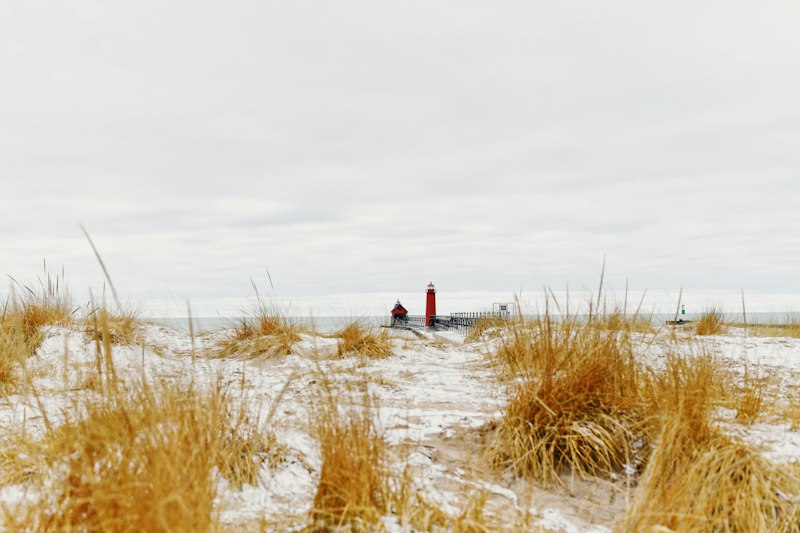 Snow-covered dunes and a red lighthouse on the Lake Michigan shore in winter